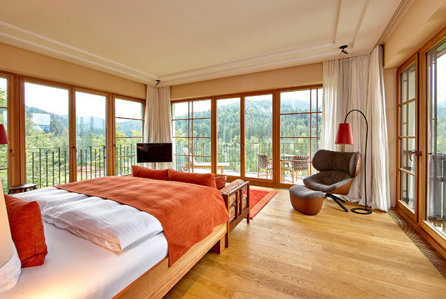 Hotelzimmer im Schloss Elmau mit Bett und Sessel und einem freien Ausblick auf die Wälder