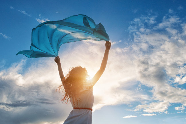 Frau mit Tuch im Wind bei sonnigem, wolkigem Himmel